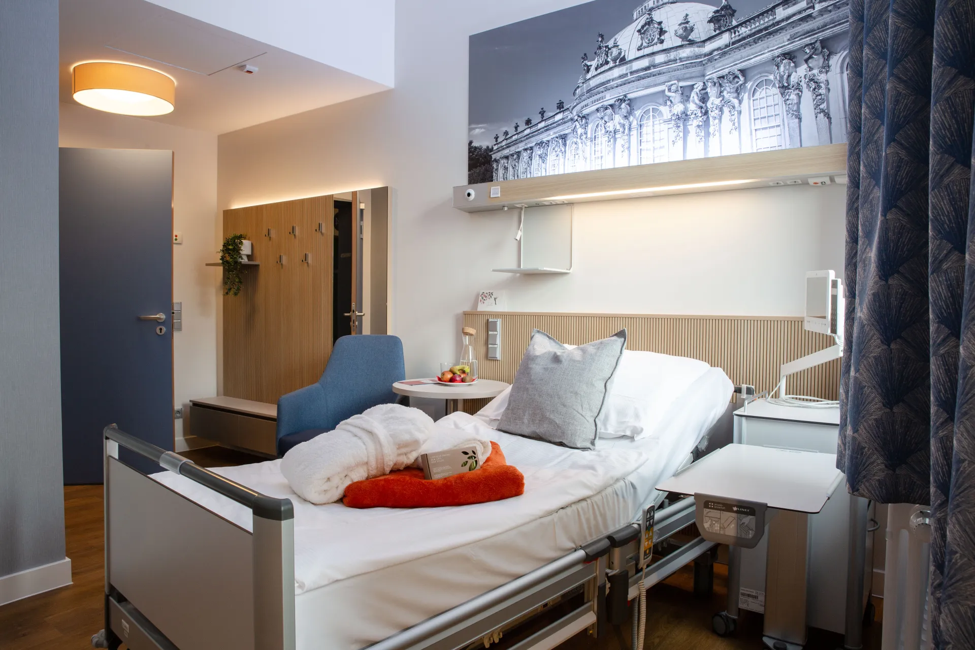 Hospital room with an adjustable bed, pillow, blanket, fruit bowl and a black-and-white photograph on the wall